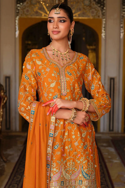 Woman in an orange traditional sharara outfit with intricate patterns in a decorated room.Woman in an orange traditional sharara outfit with intricate patterns in a decorated room.