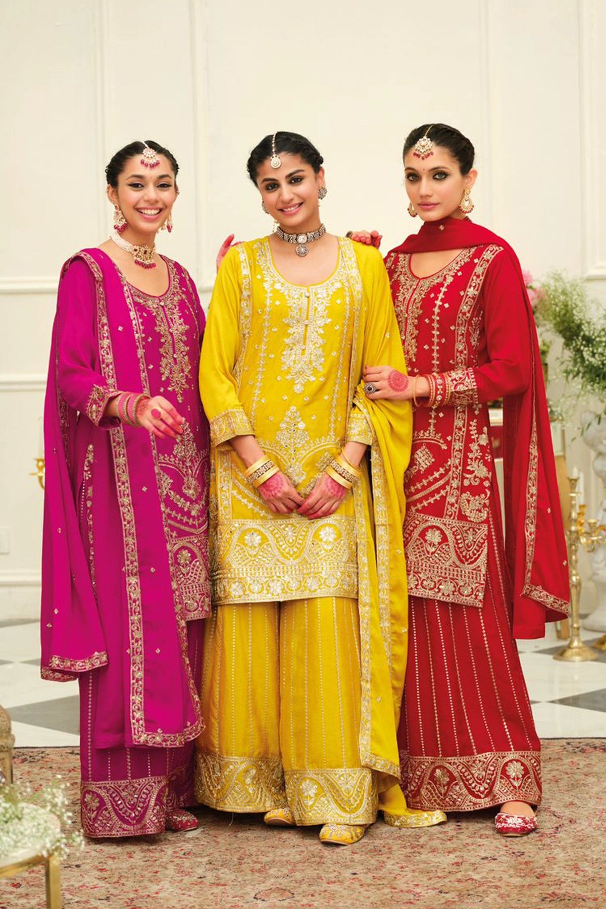 Woman wearing a red chinon silk embroidered traditional sharara outfit in an elegant indoor setting.
