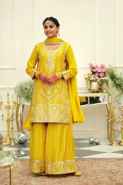 Woman in a yellow traditional sharara salwar suit outfit with intricate embroidery in an elegant indoor setting.Woman in a yellow traditional sharara salwar suit outfit with intricate embroidery in an elegant indoor setting.