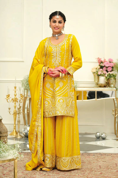 Woman in a yellow traditional sharara salwar suit outfit with intricate patterns in an elegant indoor setting.
