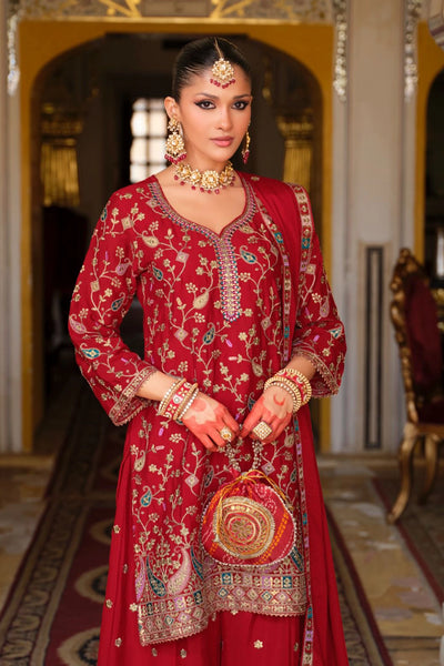 Woman in a traditional red embroidered sharara outfit standing in an ornate room.Woman in a traditional red embroidered sharara outfit standing in an ornate room.