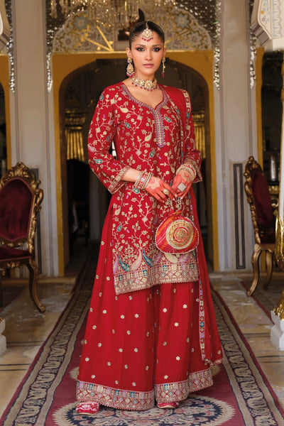 Woman in a traditional red embroidered sharara outfit standing in an ornate room.