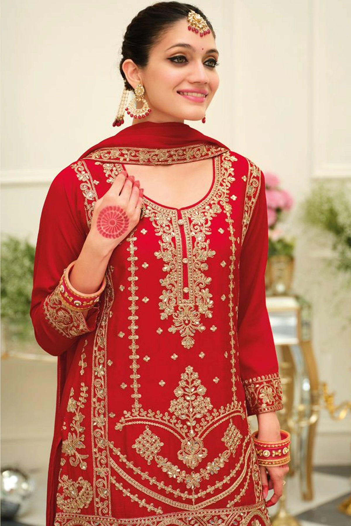 Woman wearing a red chinon silk embroidered traditional sharara outfit in an elegant indoor setting.