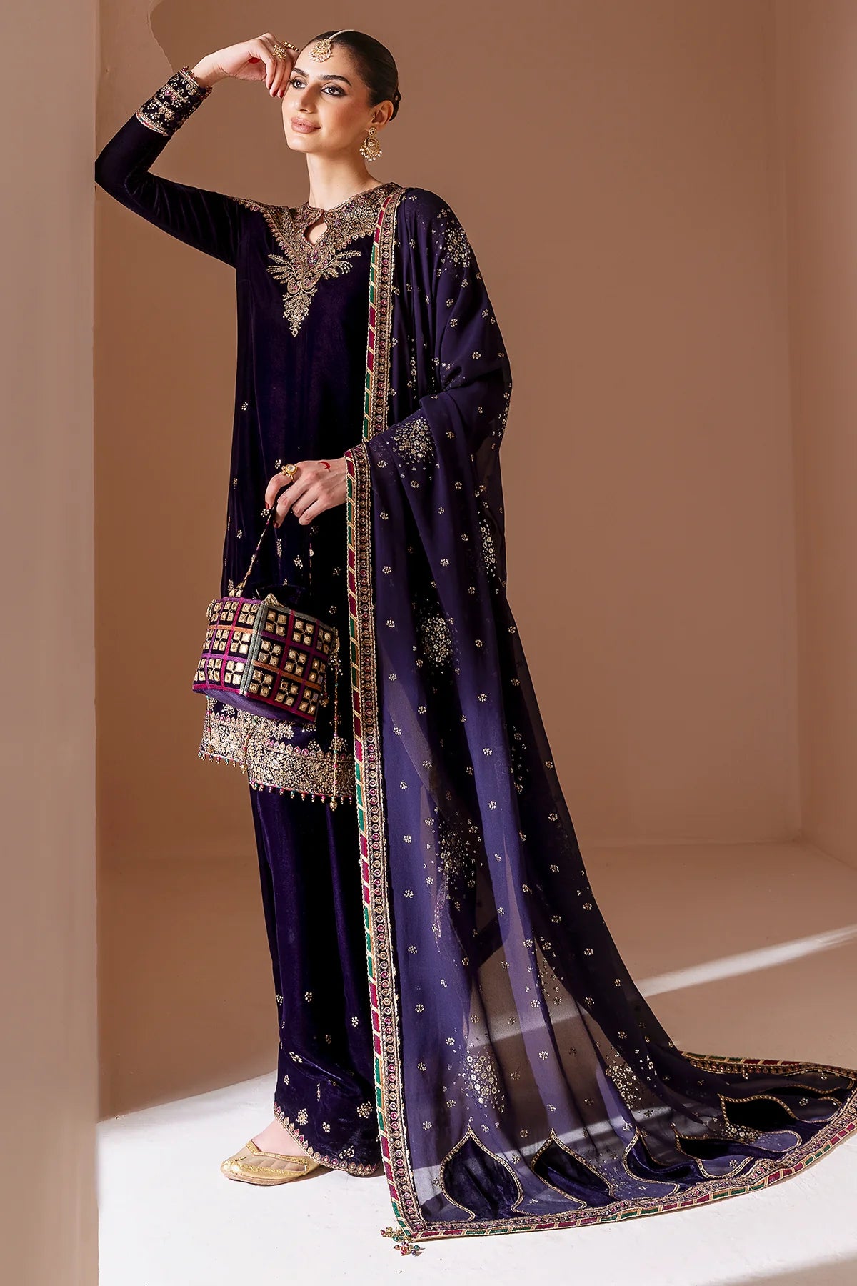 Woman wearing a traditional outfit with a dark purple dupatta and matching pants on a beige background