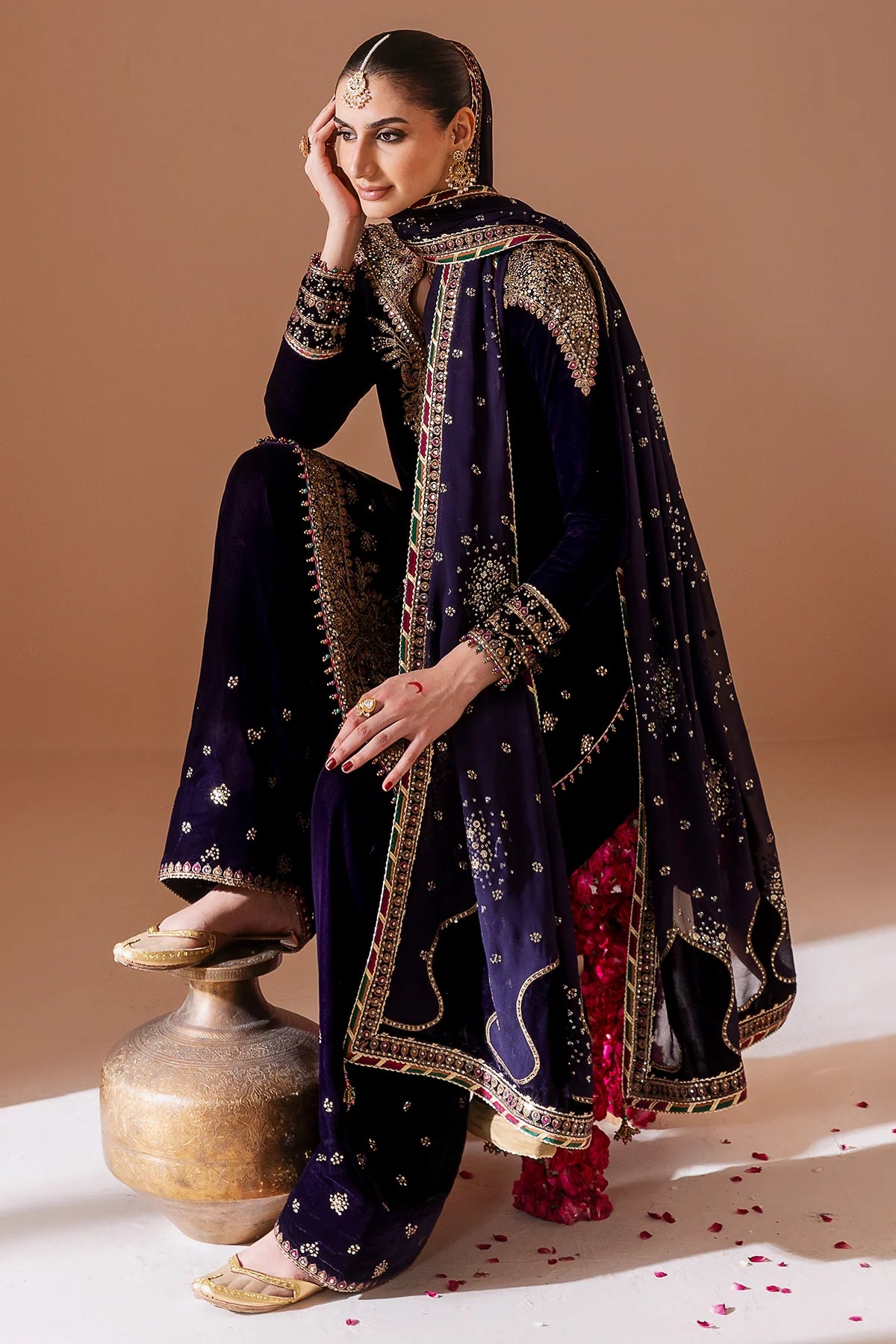 Woman in traditional attire with a dark blue dupatta and red pants on a beige background