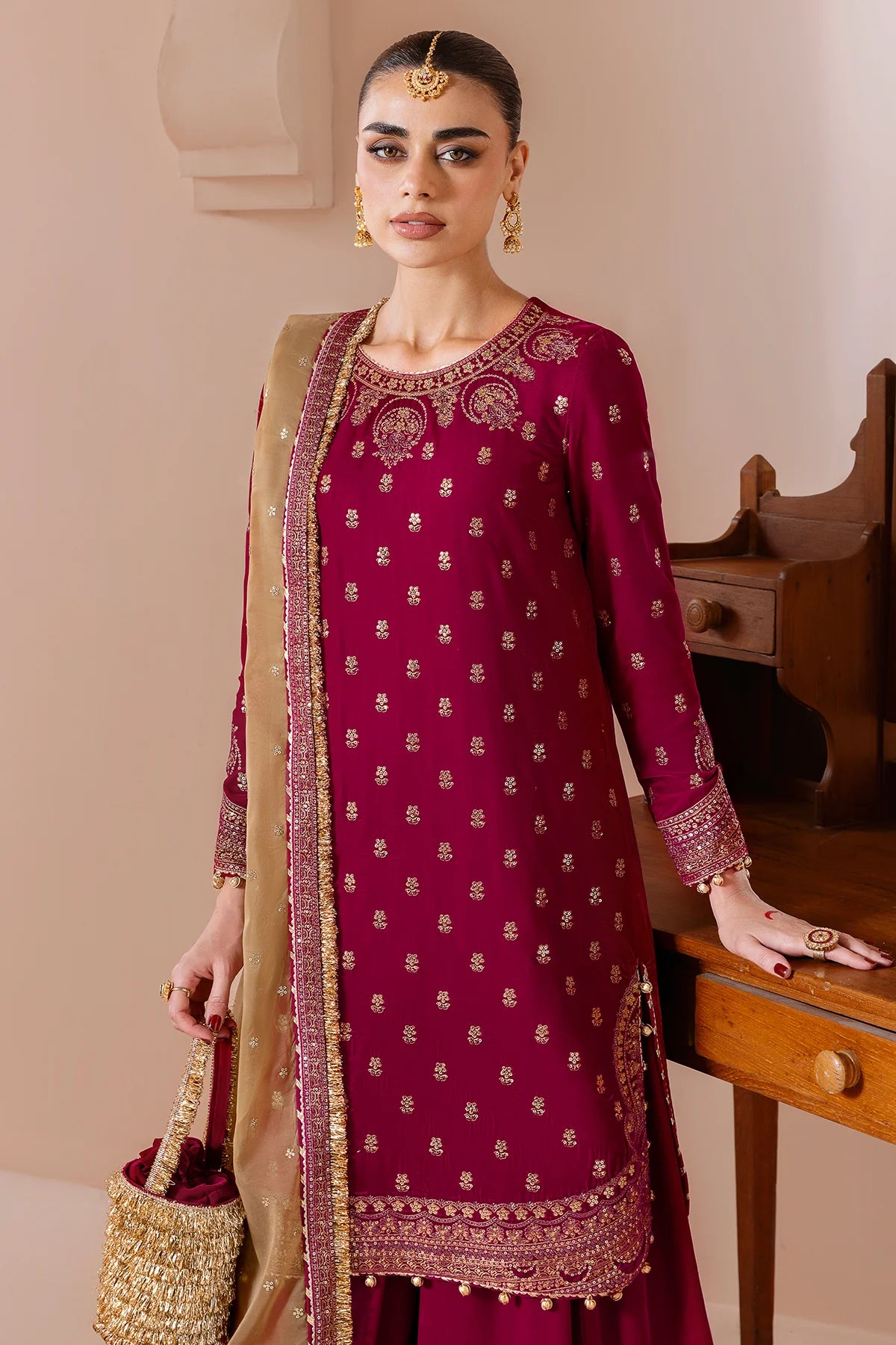 Woman wearing a maroon velvet embroidered traditional outfit with gold details indoors.