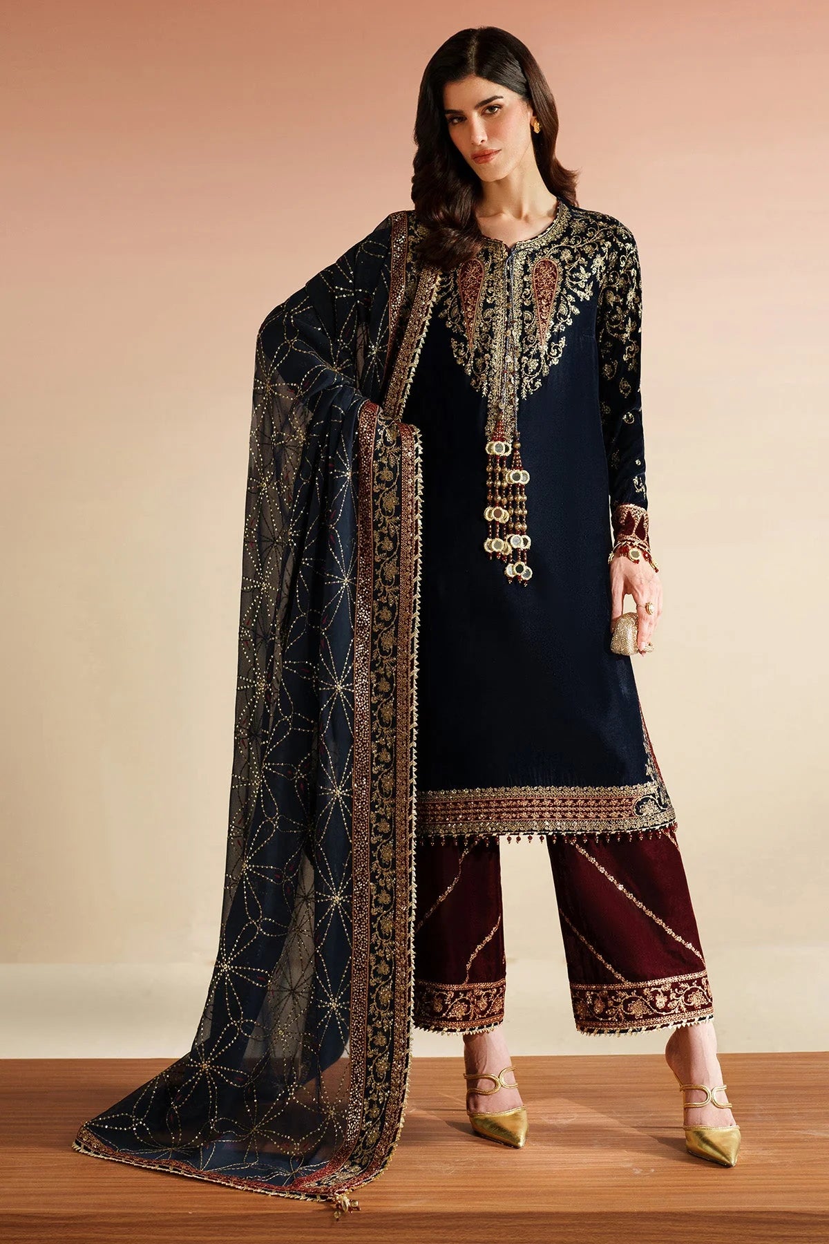 Woman wearing a traditional navy velvet kurta set outfit with a maroon pants, standing against a beige background