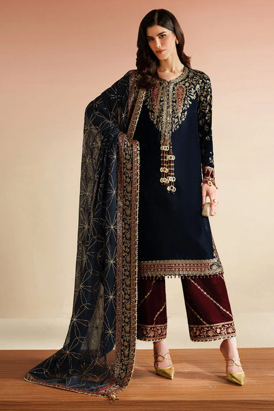 Woman wearing a traditional navy velvet kurta set outfit with a maroon pants, standing against a beige background