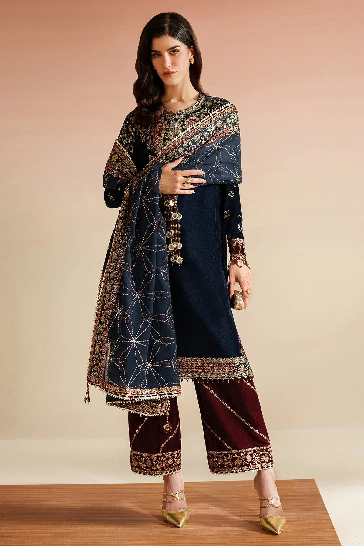 Woman wearing a traditional navy velvet kurta set outfit with a maroon pants, standing against a beige background