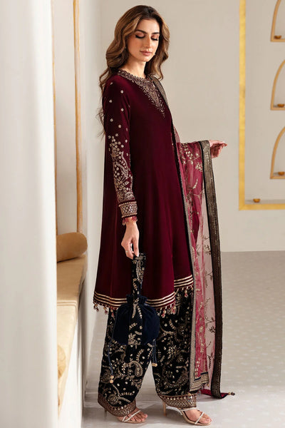 Woman in traditional maroon and navy velvet salwar suit outfit with a matching dupatta in a minimalistic setting.