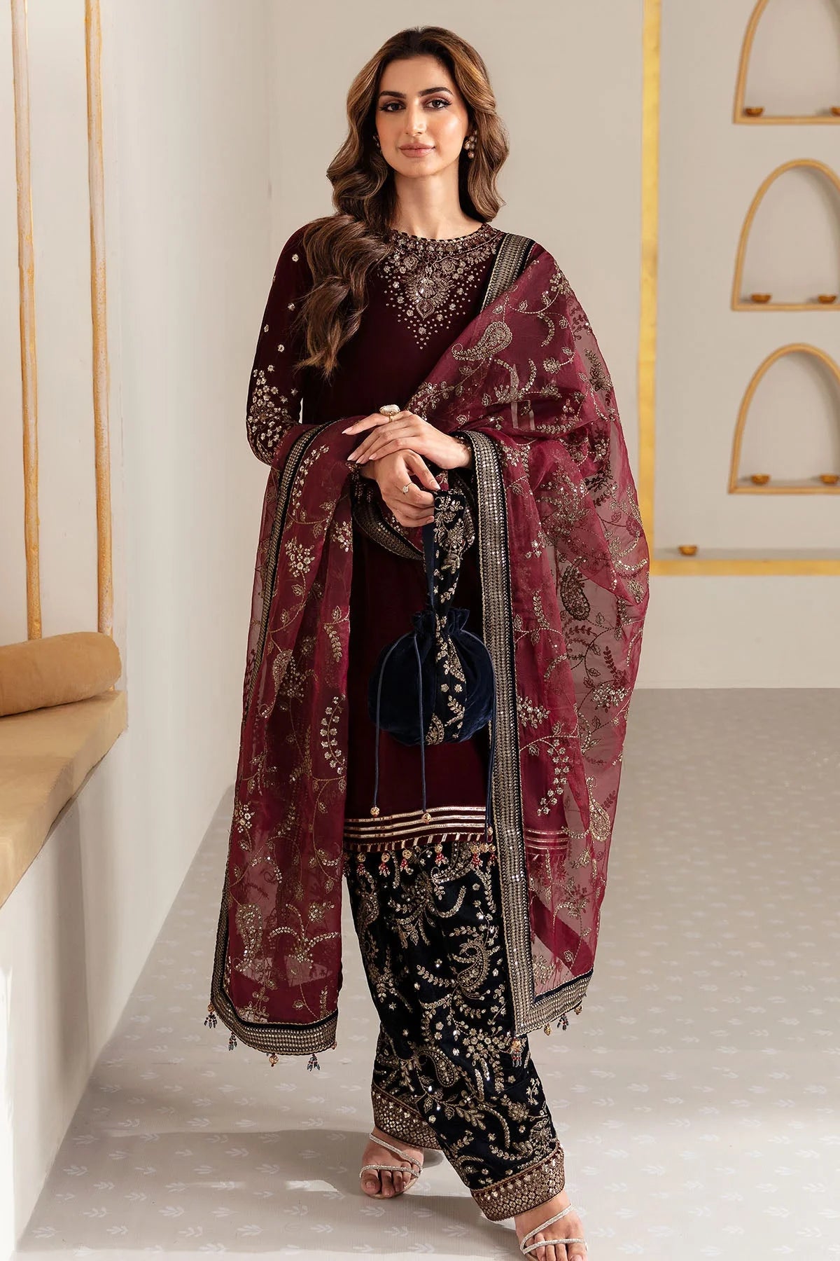 Woman in traditional maroon and navy velvet salwar suit outfit with a matching dupatta in a minimalistic setting.