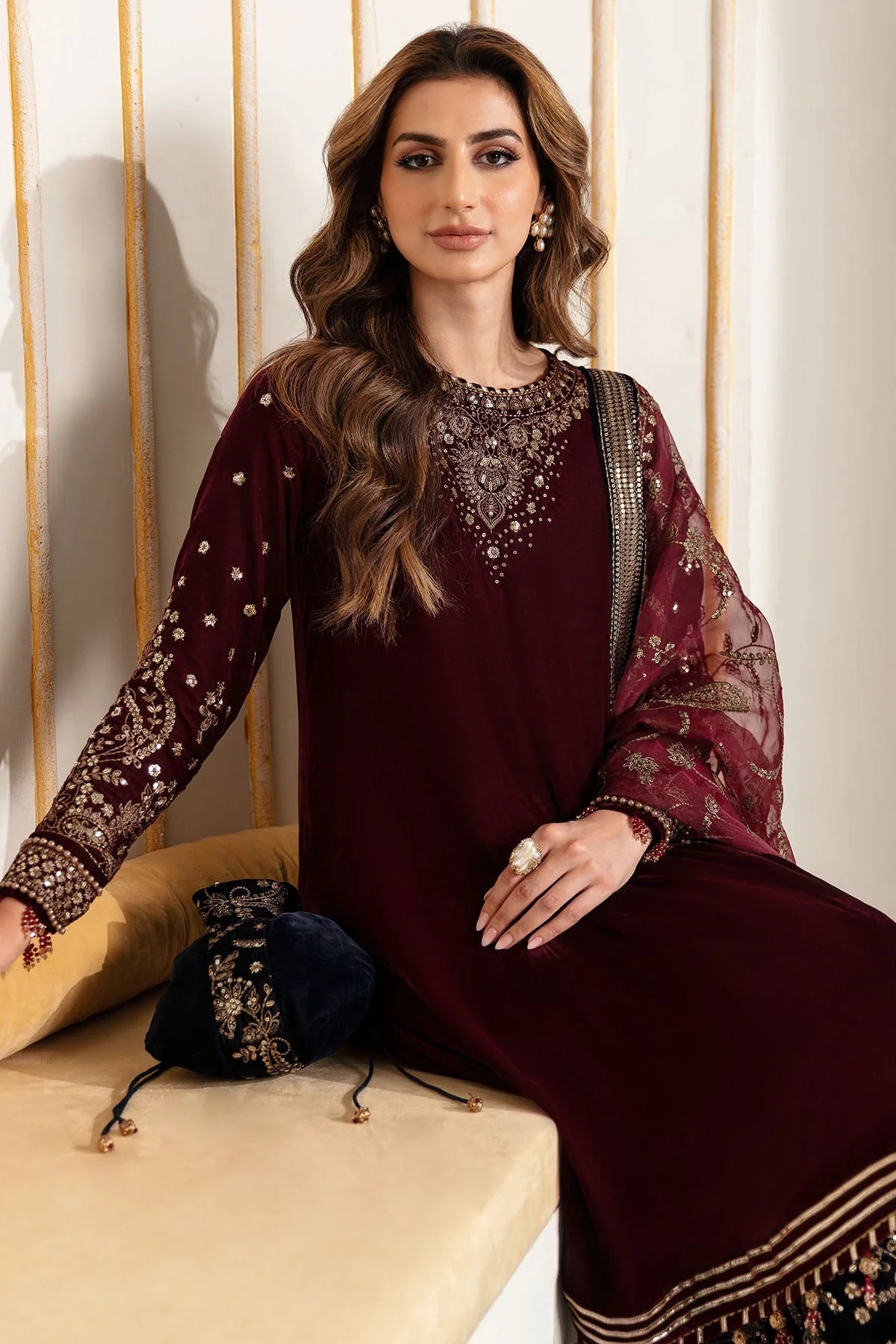 Woman in traditional maroon and navy velvet salwar suit outfit with a matching dupatta in a minimalistic setting.