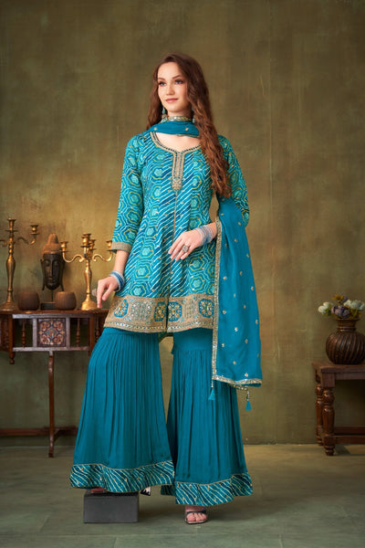 Woman wearing a teal blue traditional salwar suit outfit with gold embroidery in a studio setting.