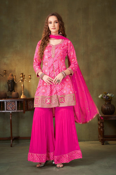 Woman wearing a bright pink traditional outfit with intricate patterns against a green background