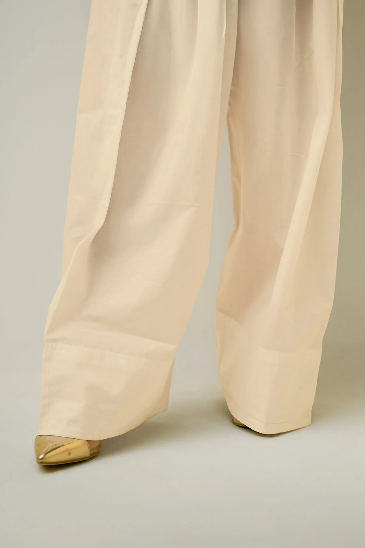 Beige farshi shalwar pants with gold shoes on a neutral background