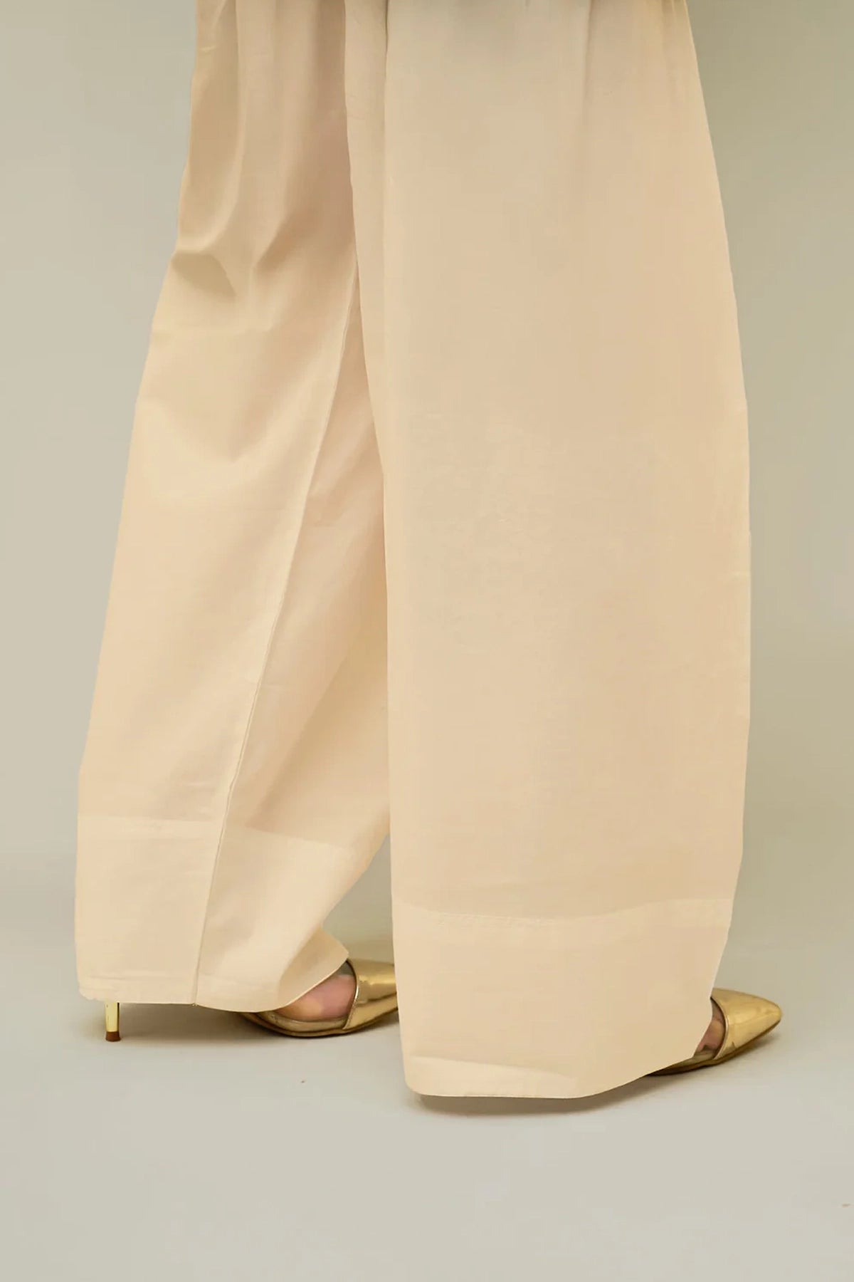 Beige farshi shalwar pants worn by a women on a plain background