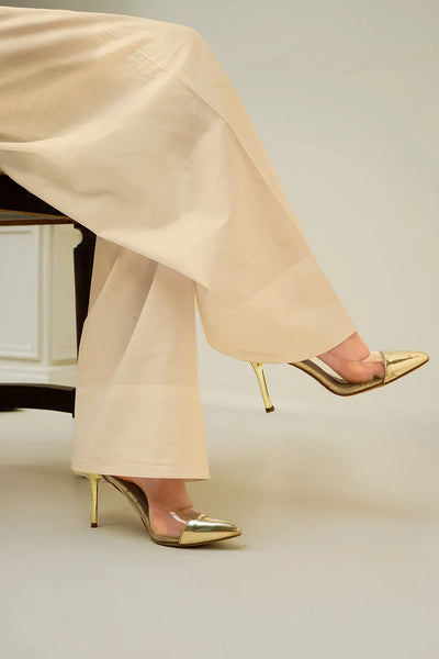 Gold high-heeled shoes worn with beige farshi patiala salwar pants on a neutral background