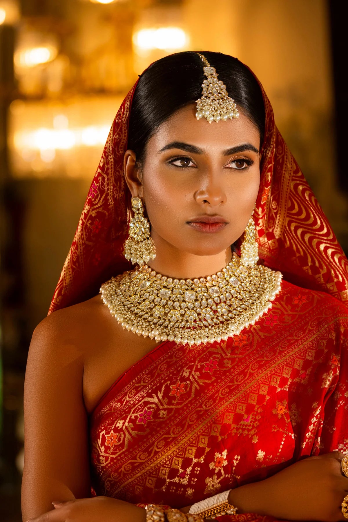 Woman in traditional red saree with gold kunan jewelry set against a warm-toned background