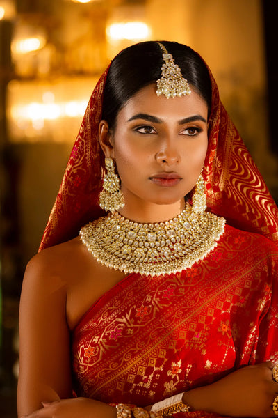 Woman in traditional red saree with gold kunan jewelry set against a warm-toned backgroundWoman in traditional red saree with gold kunan jewelry set against a warm-toned background