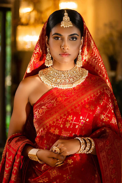 Woman in a red saree with gold bridal heavy kundan jewelry against a blurred background