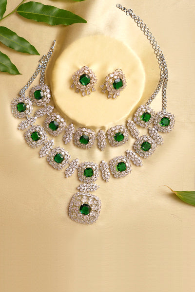 Jewelry set with necklace and earrings featuring green gemstones on a beige background.