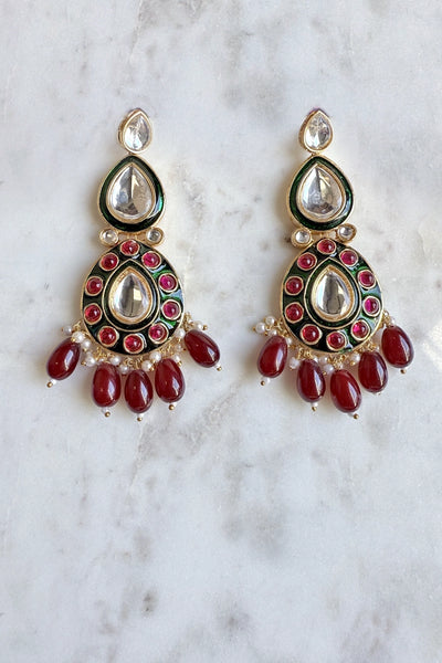 Pair of ornate earrings with red beads on a marble background