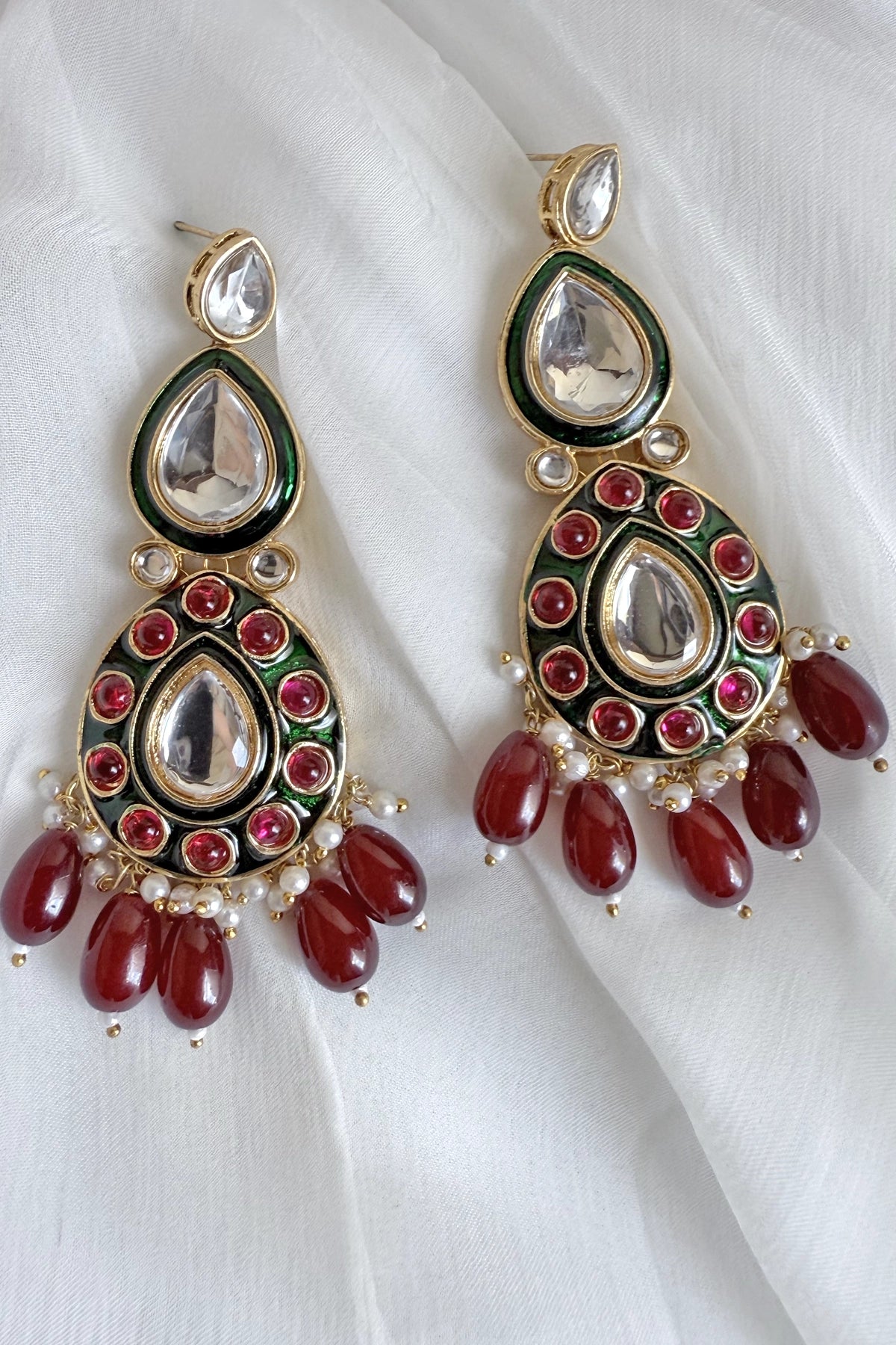 Ornate earrings with red stones and gold accents on a white fabric background