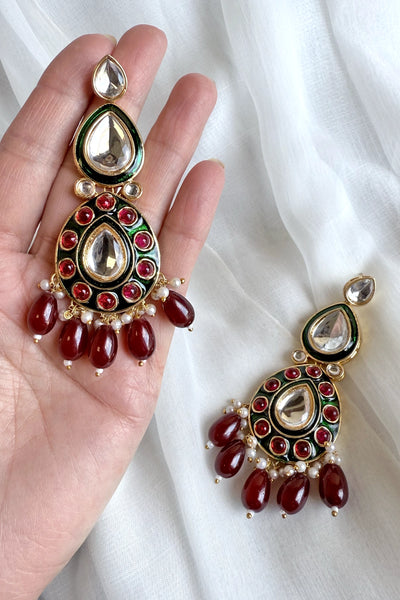 Ornate earrings with red and green stones held by a hand on a white fabric backgroundOrnate earrings with red and green stones held by a hand on a white fabric background