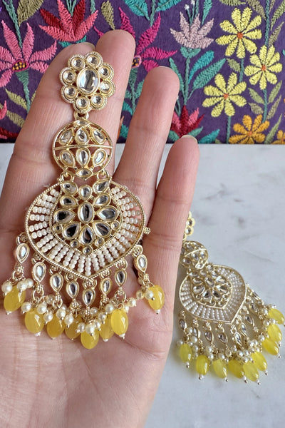 Gold and yellow jumka earrings held in a hand with a floral backgroundGold and yellow jumka earrings held in a hand with a floral background