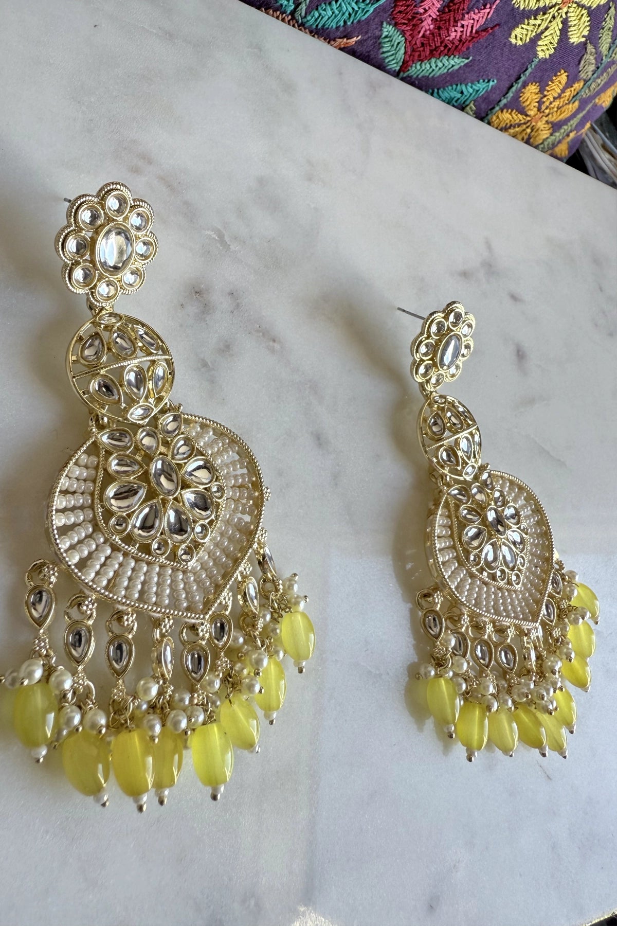 Gold and yellow jumka earrings on a marble surface with a colorful fabric background