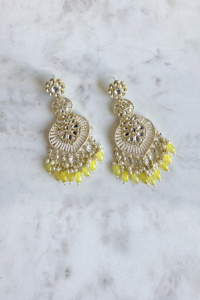Ornate jumka earrings with yellow beads on a marble surface