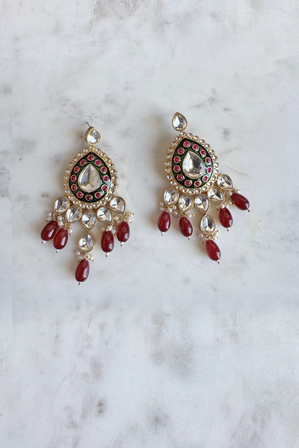 Pair of ornate earrings with red beads on a marble surface