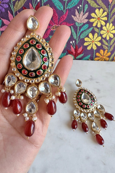 Ornate earrings with red and gold details held by a hand against a floral backgroundOrnate earrings with red and gold details held by a hand against a floral background