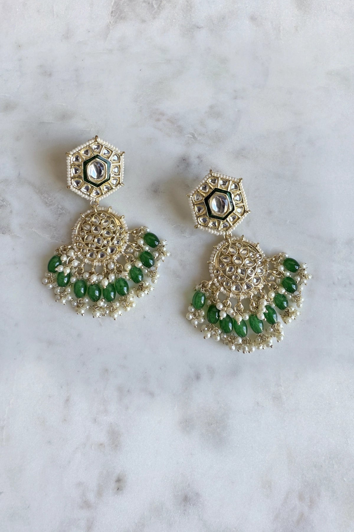 Gold and green earrings on a marble surface