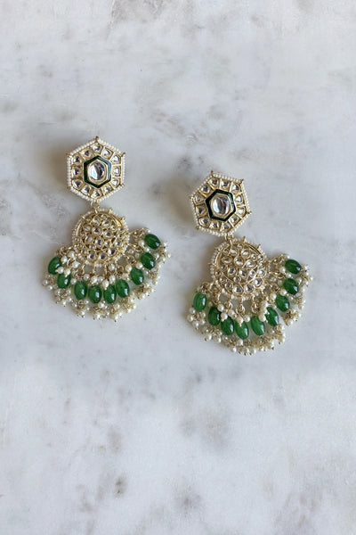 Gold and green earrings on a marble surface