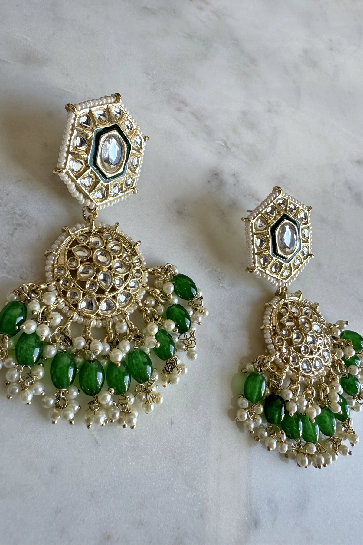Ornate earrings with green stones and gold detailing on a marble surface