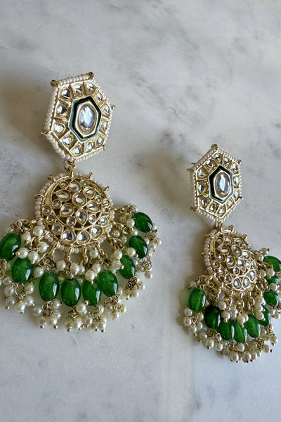 Ornate earrings with green stones and gold detailing on a marble surfaceOrnate earrings with green stones and gold detailing on a marble surface