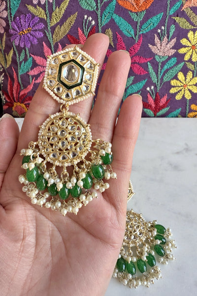 Decorative earrings with green beads held in a hand against a colorful fabric backgroundDecorative earrings with green beads held in a hand against a colorful fabric background