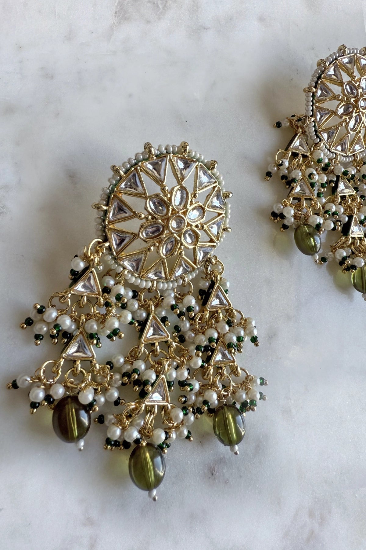 Ornate gold and green earrings on a marble surface