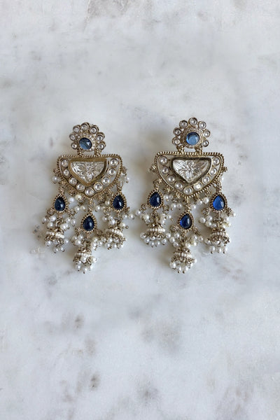 Ornate earrings with blue stones and pearl-like elements on a marble surface
