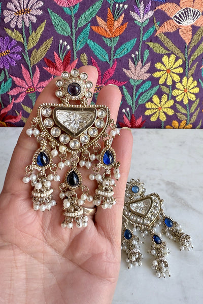 Ornate earrings with pearls and gemstones held in a hand against a floral fabric backgroundOrnate earrings with pearls and gemstones held in a hand against a floral fabric background