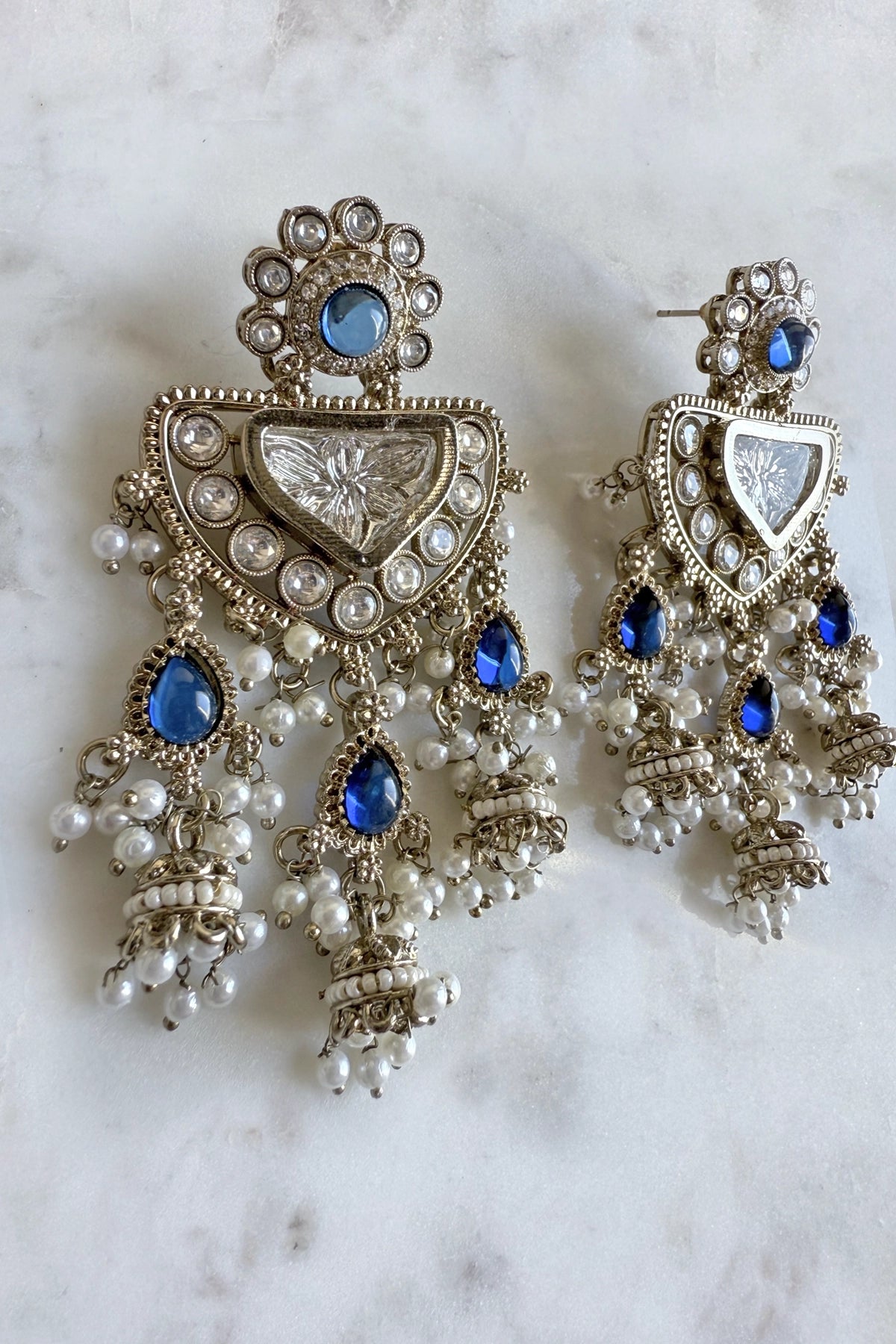 Ornate earrings with blue stones and pearl-like beads on a marble background