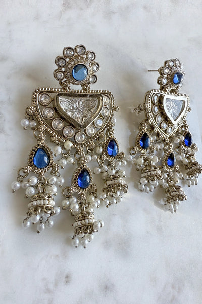 Ornate earrings with blue stones and pearl-like beads on a marble backgroundOrnate earrings with blue stones and pearl-like beads on a marble background