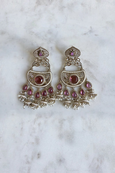 Ornate silver earrings with purple and pink gemstones on a marble surface