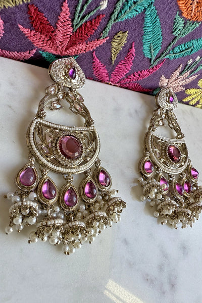 Ornate earrings with purple gemstones on a marble surface with a colorful embroidered fabric background.Ornate earrings with purple gemstones on a marble surface with a colorful embroidered fabric background.