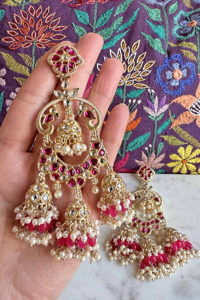 Gold and pink earrings held by a hand with a colorful embroidered fabric backgroundGold and pink earrings held by a hand with a colorful embroidered fabric background