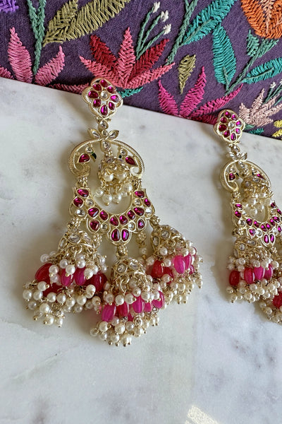 Jumka earrings with pink and white pearls, and stones on a marble surface with an embroidered fabric background.Jumka earrings with pink and white pearls, and stones on a marble surface with an embroidered fabric background.