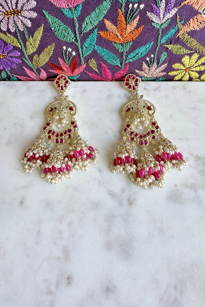 Jumka earrings with pink and gold details on a marble surface with a colorful fabric background.Jumka earrings with pink and gold details on a marble surface with a colorful fabric background.