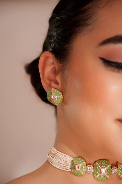 Close-up of a women wearing Gold Finish Green Stones Kundan Polki Necklace And Earring Set against a neutral background.Close-up of a women wearing Gold Finish Green Stones Kundan Polki Necklace And Earring Set against a neutral background.