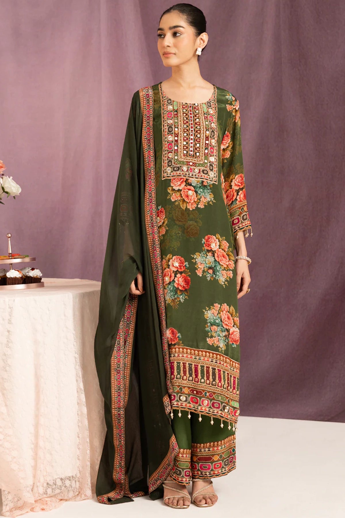 Woman wearing a traditional embroidered green dress with a matching dupatta against a purple background